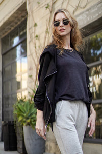 Woman wearing sunglasses and a black jacket over a black striped tee with gray pants in an urban setting