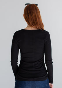 Person wearing a black long-sleeve top and blue jeans on a plain background