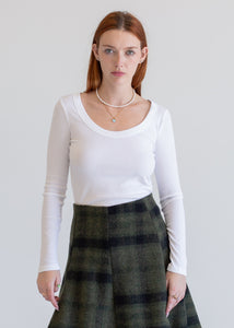 Woman wearing a white long-sleeve top and plaid skirt against a plain background