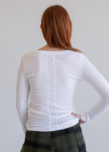 Woman wearing a white long-sleeve top with a plain background