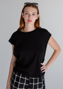 Woman wearing a black t-shirt and plaid pants against a gray background