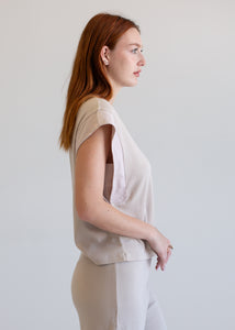 Woman wearing a beige sleeveless top and white pants against a plain background