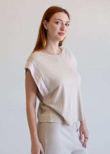 Woman wearing a beige top and white pants against a plain background