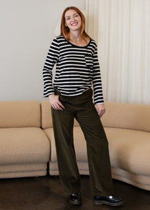 Woman wearing a black and white striped sweater and green pants standing in a living room.