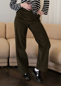 Person wearing green corduroy pants and a black and white striped shirt in front of a beige couch.