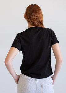 Person wearing a black t-shirt and light-colored pants against a plain background
