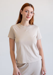 Woman wearing a beige t-shirt and pants against a plain background