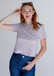Woman wearing a light purple t-shirt and blue jeans against a plain background