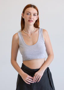 Woman wearing a gray tank top and black pants against a plain background