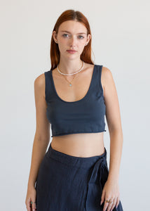 Woman wearing a navy blue sleeveless top and dark pants against a plain background
