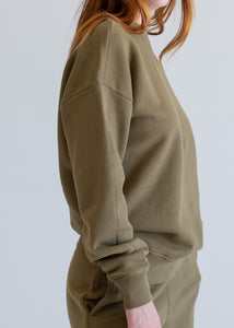 Person wearing a green sweatshirt and pants on a light gray background