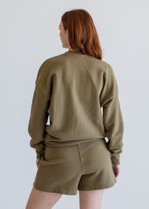 Person wearing an olive green sweatshirt and shorts set on a plain background