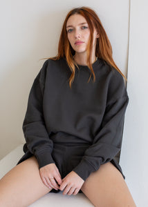 Woman wearing a black oversized sweatshirt sitting on a white surface.