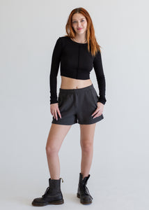 Person wearing a black long-sleeve top and black shorts on a white background
