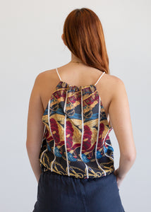 Woman wearing a colorful patterned top with thin straps on a plain background
