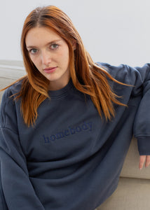 Person wearing a navy blue 'homebody' sweatshirt sitting on a couch.