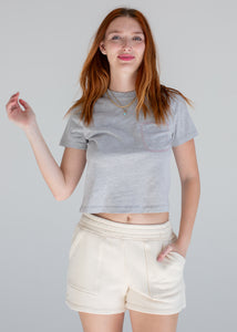 Woman wearing a gray crop top and beige shorts against a plain background