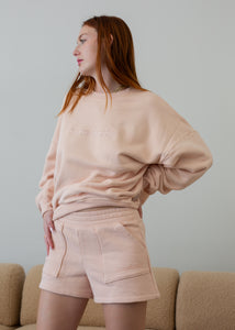 Woman wearing a light pink sweatshirt and shorts set against a plain background