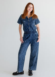Woman wearing a denim jumpsuit on a plain background