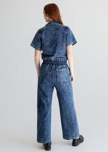 Person wearing a blue denim jumpsuit on a light gray background