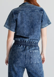 Person wearing a blue denim jumpsuit on a plain background