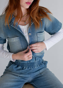 Person wearing a blue denim outfit with a white shirt underneath on a plain background