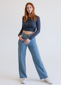 Woman wearing a dark blue long-sleeve top and light blue jeans on a white background