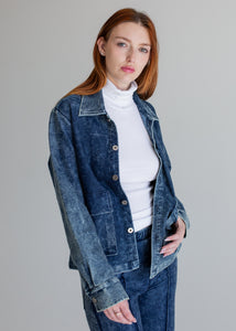 Woman wearing a blue denim jacket over a white turtleneck on a gray background