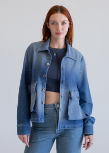 Woman wearing a blue denim jacket and jeans against a plain background