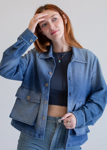 Woman wearing a blue denim jacket and jeans against a plain background