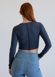 Person wearing a dark blue long-sleeve top and light blue jeans against a plain background