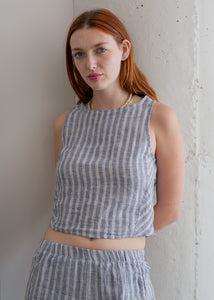 Woman wearing a blue and white striped outfit against a plain wall.