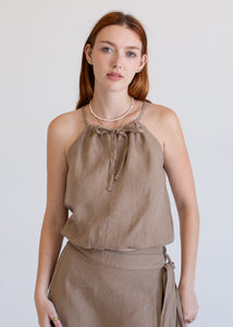 Woman wearing a beige sleeveless top and skirt set against a plain background
