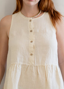 Beige sleeveless dress with buttons worn by a person against a neutral background