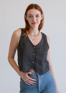 Woman wearing a vintage black vest with buttons and blue jeans against a plain background