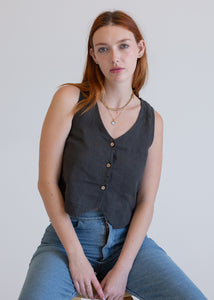 Woman wearing a vintage black vest and blue jeans sitting against a plain background