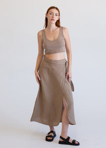 Woman wearing a beige tank top and long skirt against a white background