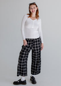 Person wearing a white long-sleeve top and black and white checkered pants on a plain background