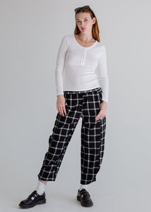Woman wearing a white long-sleeve top and black and white checkered pants on a gray background