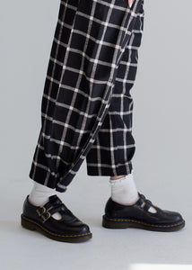 Person wearing black checkered pants and black shoes on a plain background