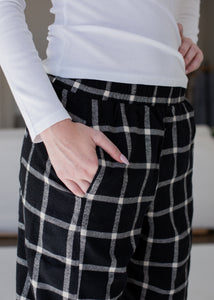 Person wearing black plaid pants with a white top indoors.
