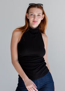 Woman wearing a black sleeveless top and blue jeans against a gray background