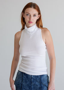 Woman wearing a white sleeveless top and blue jeans against a plain background