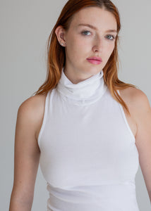 Woman wearing a white sleeveless top against a plain background