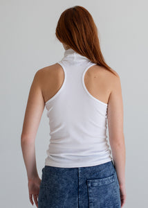 Person wearing a white tank top and blue jeans against a plain background