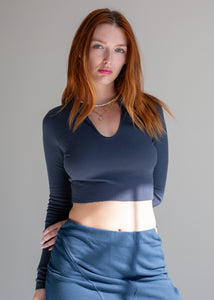Woman wearing a dark blue long-sleeve top and blue pants against a gray background