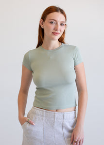 Woman wearing a sage t-shirt and light gray pants against a white background