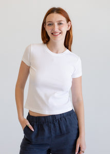 Woman wearing a white t-shirt and dark pants against a plain background