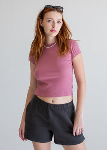 Woman wearing a mauve t-shirt and black shorts against a plain background