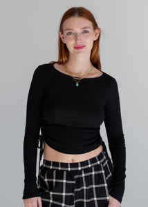 Woman wearing a black long-sleeve top and plaid pants against a gray background